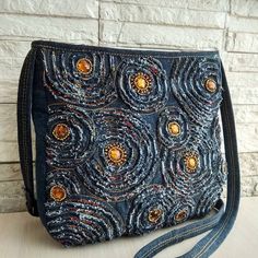 a handbag made with denim and beading on the front, sitting against a brick wall