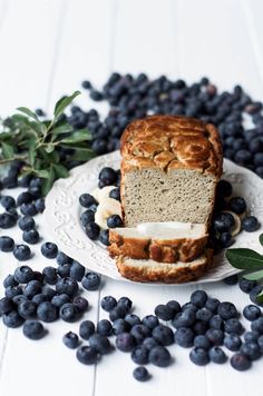 a loaf of bread with blueberries on a plate next to some leaves and berries