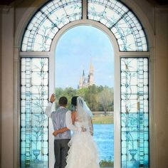 a bride and groom standing in front of a stained glass window looking at the water