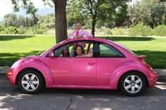 a man and woman sitting in the back of a pink beetle car with their baby