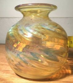 a yellow glass vase sitting on top of a wooden table next to a measuring tape