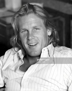 a black and white photo of a man with long hair wearing a striped shirt smiling