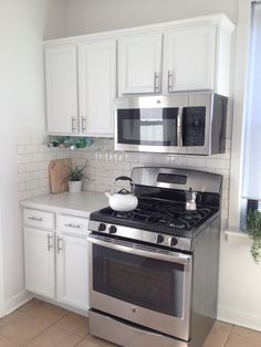 a stainless steel stove and microwave in a kitchen with white cabinets, tile flooring and tiled walls