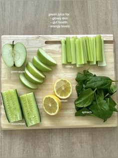 a cutting board topped with sliced up green apples and cucumbers next to slices of lemon