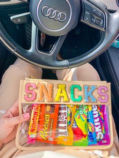 someone is holding up some snacks in their car's steering wheel compartment, with the word snack on it