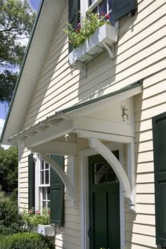 a white house with green shutters and flowers in the window boxes on the front