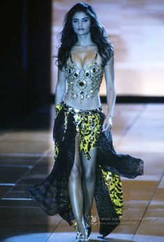 a woman in a yellow and black outfit walking down a runway with an animal print skirt