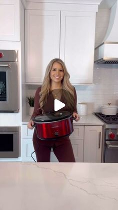 a woman standing in a kitchen holding a red crock pot