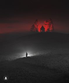 a person standing on a hill at night in the fog with a red light behind them