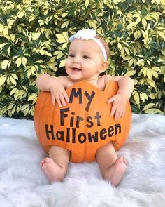 a baby sitting on top of a pumpkin with the words my first halloween written on it