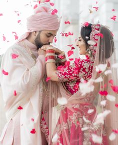 a man and woman standing next to each other with petals in the air around them