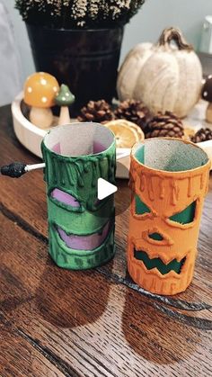 two paper cups sitting on top of a wooden table next to pine cones and pumpkins