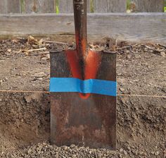 a shovel with a blue stripe on it sitting in the dirt next to a fence