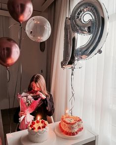 a woman is holding a birthday cake and blowing out the candles on it with balloons in the background