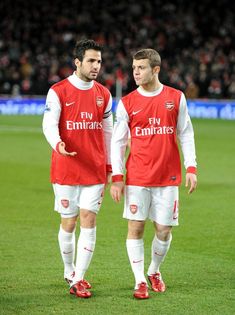 two men in red and white soccer uniforms standing on a field with one man looking at the camera