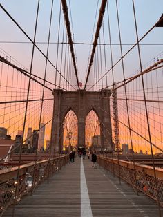 people walking across the brooklyn bridge at sunset