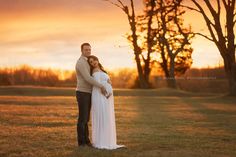 a pregnant couple standing in the grass at sunset