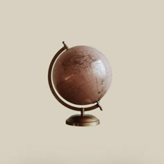 a small globe on a stand with a white wall in the back ground and a light brown background