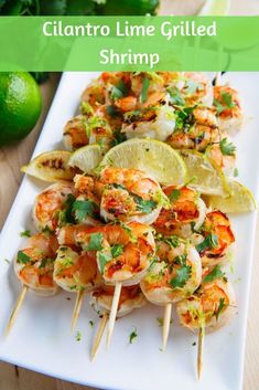 grilled shrimp skewers with lime wedges and cilantro on a white plate