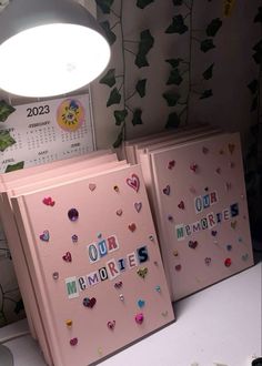 two pink notebooks with hearts and the word our memories written on them next to a lamp