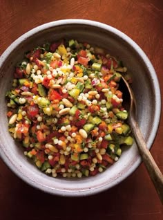 a bowl filled with corn and vegetables on top of a wooden table next to a spoon