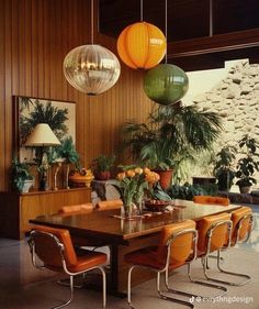 a dining room table surrounded by orange chairs and hanging lights over it's head