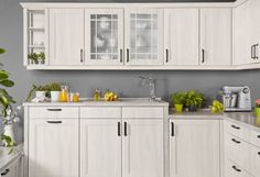 a kitchen filled with lots of white cupboards and counter top space next to a potted plant