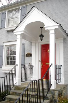 a red door sits in front of a white house with black railings and stairs