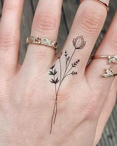 a woman's hand with three different tattoos on her fingers and two rings in the middle