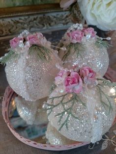 some white balls with pink flowers on them sitting in a glass bowl next to a mirror