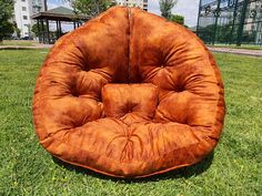 a brown chair sitting on top of a green grass covered field next to a park