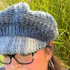 a close up of a person wearing a knitted hat and eyeglasses with grass in the background