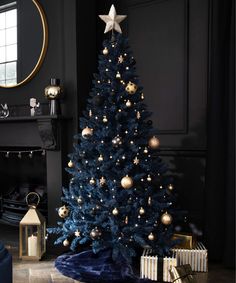 a blue christmas tree with gold ornaments in a black living room decorated for the holidays