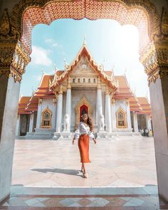 a woman standing in front of a building with columns and arches on the floor, looking into the camera