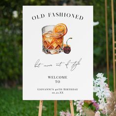 an old fashioned welcome sign is displayed in front of flowers and greenery with a cocktail on it