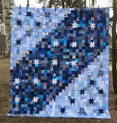 a blue and white quilt hanging from a tree in the woods with stars on it