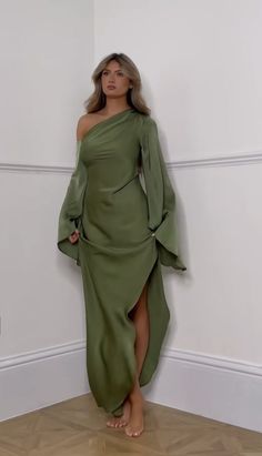 a woman in a green dress leaning against a wall