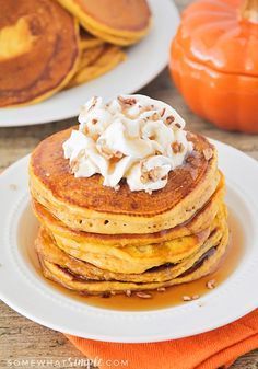 stack of pancakes with whipped cream on top and pumpkins in the backgroud