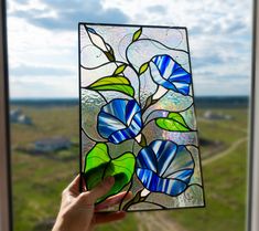 a hand holding up a stained glass window in front of a green field and blue sky