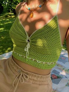 a woman wearing a green crochet top and tan shorts sitting at a picnic table