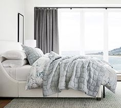 a white bed sitting next to a large window in a room with a rug on the floor