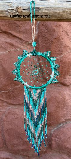 a blue and white beaded dream catcher hanging from a wooden pole with a brick wall behind it