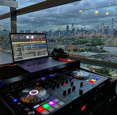 a laptop computer sitting on top of a dj's desk in front of a cityscape