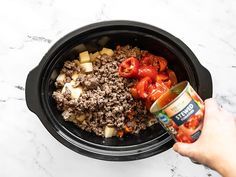 someone is holding a can of canned food in their crock pot with meat and vegetables