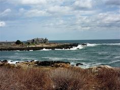 an ocean view with waves crashing on the shore and houses in the distance behind it