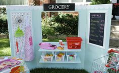 a small booth set up in the grass with baskets and food on it, along with a chalkboard sign that says grocery