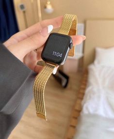 a person holding an apple watch in their hand with a gold bracelet around the wrist