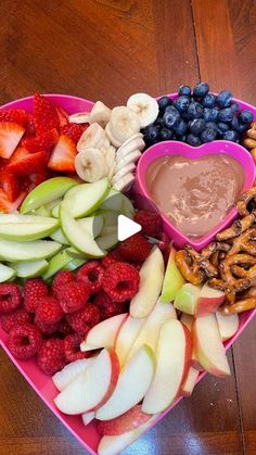 a heart shaped platter filled with fruit, pretzels, strawberries, apples, and chocolate