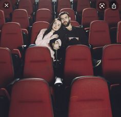 a man and woman sitting in the middle of rows of red chairs with their arms around each other