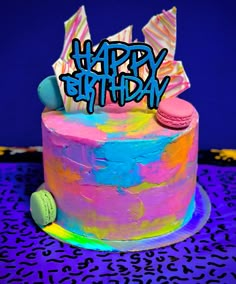 a birthday cake with the words happy birthday written on it and colorful icing, sitting on a purple tablecloth